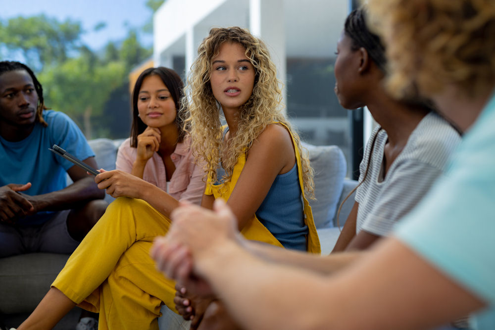 Group of diverse people sitting on sofa, using tablet and talkin