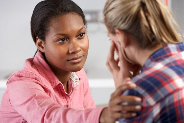 woman placing her hand on another woman's shoulder and comforting her