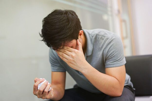 man covering his face and holding tissues